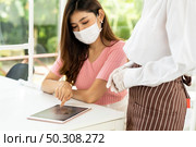 Asian waitress wear facemask and face shield using tablet to show restaurant electronic menu and recommend to customer. New normal technology and lifestyle food and dining concept. Стоковое фото, агентство Ingram Publishing / Фотобанк Лори