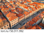 Aerial view of houses with orange roofs at sunset in summer in Dubrovnik, Croatia. Top view of beautiful architecture in old city. Historical centre, buildings, walking people on the street. Travel. Стоковое фото, агентство Ingram Publishing / Фотобанк Лори