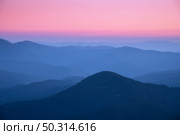 Mountain ridges in fog at sunset in autumn. Beautiful landscape with foggy mountain valley, rocks, forest, pink sky in fall at dusk in blue hour. Aerial view of hills. Top view. Nature background. Стоковое фото, агентство Ingram Publishing / Фотобанк Лори