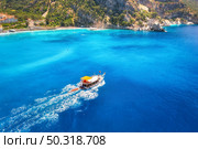 Speed boat in blue sea at sunrise in summer. Aerial view of floating motorboat in sea bay. Tropical landscape with yacht, clear water, rocks , stones, mountain, green trees. Top view. Oludeniz, Turkey. Стоковое фото, агентство Ingram Publishing / Фотобанк Лори