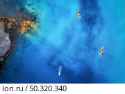 Aerial view of people on floating sup boards on blue sea, rocks, stones at sunset in summer in Oludeniz, Turkey. Tropical landscape. Kayaks on clear water. Active travel. Top view of canoe. Sport. Стоковое фото, агентство Ingram Publishing / Фотобанк Лори