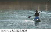 A woman sitting on her knees on a paddleboard paddling on a calm lake. She has a magnificent figure. The soft ripples reflect the sunlight. Стоковое видео, видеограф Воловодов Владимир / Фотобанк Лори
