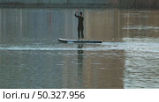 A person stands on a paddleboard, gracefully navigating the calm waters. The sunlight creates shimmering reflections on the surface, adding to the serene atmosphere. Riding the sup board. Стоковое видео, видеограф Воловодов Владимир / Фотобанк Лори