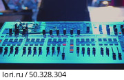 Close-up of a mixing console illuminated by blue light. Various switches, knobs and buttons are visible, showing a professional setup. There is a live performance in the background. Стоковое видео, видеограф Воловодов Владимир / Фотобанк Лори