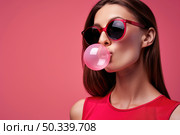 Charming woman with sunglasses on is blowing a bubble, showing a fun and playful moment captured in the frame. Стоковое AI-изображение, AI-художник Данила Большаков / Фотобанк Лори