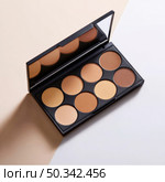 Open contour and concealer makeup palette with mirror, displaying warm skin tones, ideal for beauty, cosmetics, and skincare visuals in a clean setting. Стоковое AI-изображение, AI-художник Катерина Бондарец / Фотобанк Лори