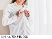 smiling young woman putting button her white shirt. Стоковое фото, агентство Ingram Publishing / Фотобанк Лори
