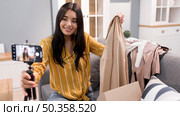 female vlogger home with smartphone unboxing clothes. Стоковое фото, агентство Ingram Publishing / Фотобанк Лори