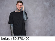 smiling portrait tattooed young man with pierced ears talking mobile phone. Стоковое фото, агентство Ingram Publishing / Фотобанк Лори
