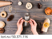 female hand tying glass bottle with string near cutter dry lotus pod dried fruit slices pine cone textured wooden surface. Стоковое фото, агентство Ingram Publishing / Фотобанк Лори
