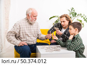 focused multi generational family assembling jigsaw puzzle together. Стоковое фото, агентство Ingram Publishing / Фотобанк Лори