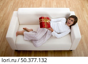 Woman in pajama seated on a sofa holding a Christmas gift. Стоковое фото, агентство Ingram Publishing / Фотобанк Лори