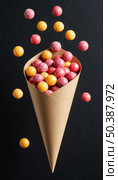 Kraft paper bag with scattered dragee candies on black background. Стоковое AI-изображение, AI-художник Анна Никонорова / Фотобанк Лори