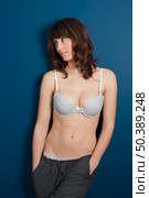 Beautiful young woman wearing a casual lingerie and pajama pants, against a blue wall. Стоковое фото, агентство Ingram Publishing / Фотобанк Лори
