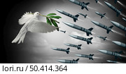 Against the war concept as a white dove holding an olive branch facing off against a group of bombs and missiles as a symbol for diplomatic agreement to avoid fighting with 3D elements. Стоковое фото, агентство Ingram Publishing / Фотобанк Лори