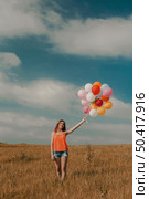 Beautiful young woman walking on meadow holding ballons. Стоковое фото, агентство Ingram Publishing / Фотобанк Лори