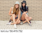 Two beautiful and young girlfriends having fun with a skateboard, in front of a brick wall. Стоковое фото, агентство Ingram Publishing / Фотобанк Лори