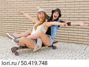 Two beautiful and young girlfriends having fun with a skateboard, in front of a brick wall. Стоковое фото, агентство Ingram Publishing / Фотобанк Лори