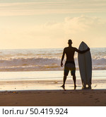 Surfer on the beach holding is surfboard and checking the waves. Стоковое фото, агентство Ingram Publishing / Фотобанк Лори