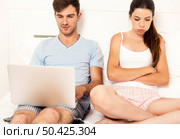 Addicted young man on bed with a laptop while the woman looks angry. Стоковое фото, агентство Ingram Publishing / Фотобанк Лори