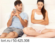 Addicted young man on bed with a cellphone while the woman looks angry. Стоковое фото, агентство Ingram Publishing / Фотобанк Лори