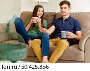 Young couple on the sofa drinking coffee while watching tv. Стоковое фото, агентство Ingram Publishing / Фотобанк Лори
