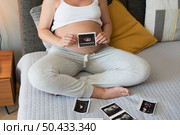 Pregnant woman holding the picture of the ultrasound on her belly in bed at home. Prenatal health care concept. Стоковое фото, агентство Ingram Publishing / Фотобанк Лори
