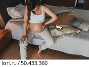 Painful pregnant young woman at home calling medical assistance on phone . Стоковое фото, агентство Ingram Publishing / Фотобанк Лори
