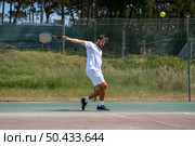Tennis player hitting backhand at ball with racket on court. Стоковое фото, агентство Ingram Publishing / Фотобанк Лори