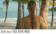 Woman with braid looking at the sea on sandy beach through palm trees in Mexico. Стоковое видео, видеограф Igor Tichonow / Фотобанк Лори