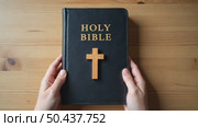 Close up of a person's hands holding the Holy Bible with a wooden cross on a table. Concept of Christian faith, spirituality, and worship. Стоковое AI-видео, аниматор Sergey Grishin / Фотобанк Лори