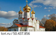 A majestic white Orthodox church with golden domes stands in a park with colorful autumn trees under a blue sky with clouds. Стоковое AI-видео, аниматор Sergey Grishin / Фотобанк Лори