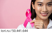 The close up photo shows an Asian woman with black hair and a bright smile holding a pink ribbon. The delicate pink background symbolizes support in the fight against breast cancer. Стоковое AI-изображение, AI-художник Светлана  Громак / Фотобанк Лори