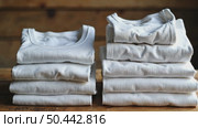 Neatly folded white t-shirts stacked on a wooden surface. Many folded white basic cotton linen presented in rustic interior. Minimalist clothing organization and clean laundry concept. Стоковое AI-видео, аниматор Sergey Grishin / Фотобанк Лори