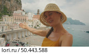 Smiling woman gestures toward colorful cliffside buildings in Amalfi Italy during summer trip. Стоковое видео, видеограф Igor Tichonow / Фотобанк Лори