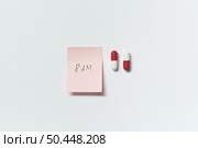 Sticky note with time and pharmaceutical tablets and over white backdrop.. Sticky note and pharmaceutical tablets. Стоковое фото, агентство Ingram Publishing / Фотобанк Лори