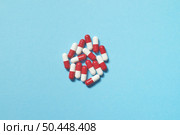 Red and white pharmaceutical tablets scattered over blue backdrop, copy space. Health care and medication-assisted treatment.. Pharmaceutical tablets over blue backdrop. Стоковое фото, агентство Ingram Publishing / Фотобанк Лори