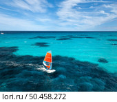 Aerial view of windsurfer on blue sea at sunny summer day. Windsurfing. Extreme sport and vacation. Top view of man on windsurfer board, waves, clear azure water in Sardinia, Italy. Tropical landscape. Стоковое фото, агентство Ingram Publishing / Фотобанк Лори