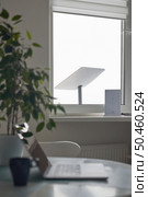 KYIV, UKRAINE - JANUARY 24, 2023: Starlink antenna and wi-fi router on windowsill in home office interior with laptop on table with cup of coffee in foreground, selective focus. Редакционное фото, агентство Ingram Publishing / Фотобанк Лори