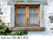 A close-up of an old wooden window with peeling paint in the frame, installed in a white stone wall. The window consists of two sashes with vertical and horizontal sashes, behind which light translucent curtains are visible. In the lower corner of the frame, climbing grapes grow, giving the scene a cozy and rustic charm. The atmosphere of the image conveys a sense of peace, antiquity and rural coziness. Suitable for themes of architecture, rustic style, vintage decor and the history of everyday life. Стоковое AI-изображение, AI-художник Анна Кривицкая / Фотобанк Лори
