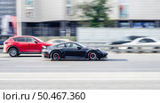 Two cars race along the road at high speed. Automobiles driving down the street. Black Porsche 991 and red Mazda CX-5 in motion. Редакционное фото, фотограф Константин Григорьев / Фотобанк Лори