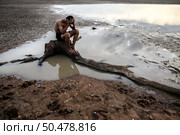 A man sat bent his knees and put his hands on his head, on the base of the tree and surrounded by water. Стоковое фото, агентство Ingram Publishing / Фотобанк Лори