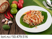 Thai papaya salad in a white plate on banana leaves with lime, tomatoes, eggplant, chili, garlic, peppers, salad, and peanuts. Стоковое фото, агентство Ingram Publishing / Фотобанк Лори
