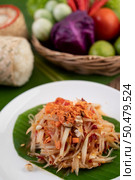 Thai papaya salad in a white plate on banana leaves with lime, tomatoes, eggplant, chili, garlic, peppers, salad, and peanuts. Стоковое фото, агентство Ingram Publishing / Фотобанк Лори