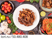 Pork cutlet in a white plate with pepper seeds, kaffir lime leaves, lemons, chilies, garlic on black cement. Стоковое фото, агентство Ingram Publishing / Фотобанк Лори