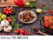 Pork cutlet in a white plate with pepper seeds, kaffir lime leaves, lemons, chilies, garlic on black cement. Стоковое фото, агентство Ingram Publishing / Фотобанк Лори
