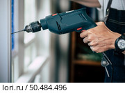 The carpenter holds the drill and drills the window. Selective focus. Стоковое фото, агентство Ingram Publishing / Фотобанк Лори