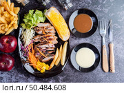 Sliced ??pork steak with bread, carrots, cauliflower, lettuce and corn on a black plate on a cement floor. Стоковое фото, агентство Ingram Publishing / Фотобанк Лори