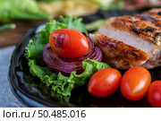 Chicken steak put on a black plate, add bell peppers, tomatoes, red onions, pineapple sauce, lettuce and sesame. Стоковое фото, агентство Ingram Publishing / Фотобанк Лори