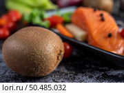 Raw salmon fillets, pepper, kiwi, pineapples, and rosemary onto a plate and black cement floor.Selective focus kiwi. Стоковое фото, агентство Ingram Publishing / Фотобанк Лори